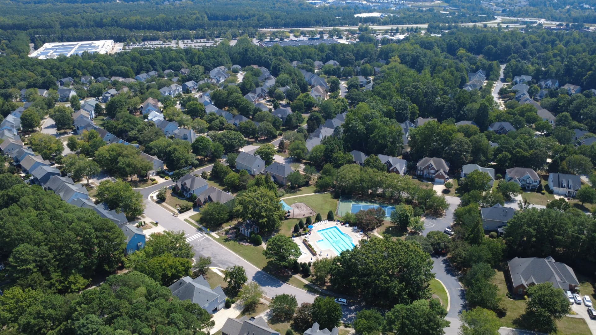 Aerial view of the wooded Crenshaw Hall area with homes, a pool, and tennis courts