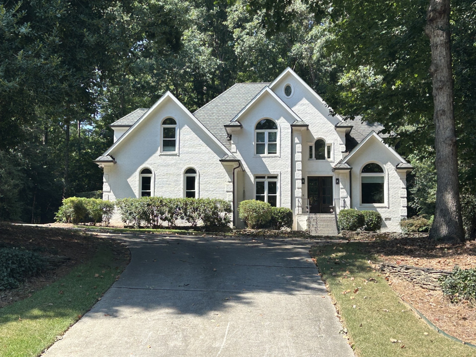 Two-story white brick home with arched windows set among mature trees in Crenshaw